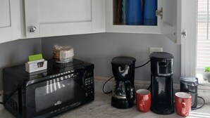 Une cuisine équipée d’un four à micro-ondes, d’une machine à café et de tasses rouges posées sur le comptoir.