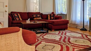 Un salon avec un canapé rouge, une petite table, un fauteuil en osier et un tapis à motifs.