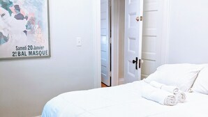 Une chambre d’hôtel avec un lit, une affiche accrochée au mur et une porte donnant sur une autre pièce.