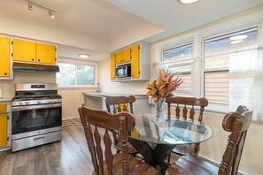A kitchen with yellow cabinets, a stainless steel stove, and a glass-top dining table with wooden chairs. - The Forrester Vista (Oak Bay North)