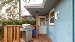 Um terraço com churrasqueira, guarda-corpo de madeira e porta para um edifício com fachada azul.