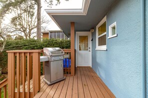 A deck with a barbecue grill, wooden railings, and a door leading to a building with a blue exterior. - The Forrester Vista (Oak Bay North)
