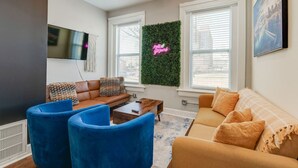 A modern living room with a brown sofa, blue armchairs, a coffee table, and a TV mounted on the wall. - Vacation stay walkable to Vanderbilt, bars and dining (Nashville)