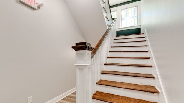 A staircase with white walls and wooden steps, leading to a landing with a window. - Vacation stay walkable to Vanderbilt, bars and dining (Nashville)