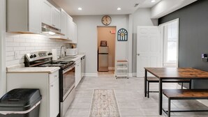 Una cocina moderna con armarios blancos, estufa de acero inoxidable y microondas. Hay una mesa de madera y una alfombra en el suelo.