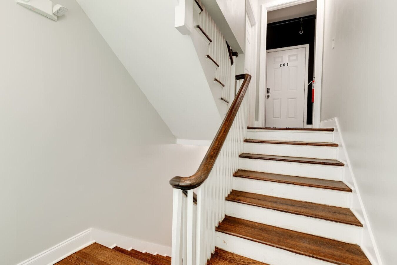 A white staircase with wooden steps and a wooden handrail, leading to a door marked with the number 201.