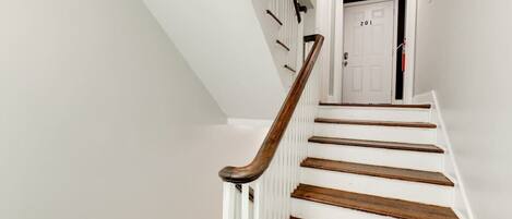 A white staircase with wooden steps and a wooden handrail, leading to a door marked with the number 201.