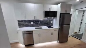A modern kitchen with white cabinets, a black tiled backsplash, stainless steel appliances, and a wooden floor.