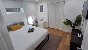 A modern bedroom with a bed, bedside table, lamp, wardrobe, and a TV on a stand.
