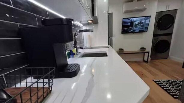 A modern kitchen with a white countertop, black appliances, and a TV mounted on the wall.
