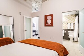 Une chambre d’hôtel comprenant un lit, une salle de bain avec des toilettes et une douche, et un couloir menant à une autre pièce.