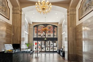 Un hall d’entrée spacieux, agrémenté d’un magnifique lustre, d’un comptoir de réception et offrant une vue sur la rue grâce à une grande porte vitrée.