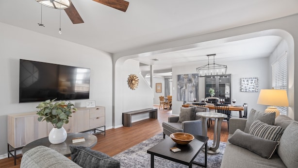 A modern living room with a large flat-screen TV, grey sofas, a coffee table, and a dining area with a chandelier. - Spacious 5BR / Perfect for Families & Groups (Universal City)