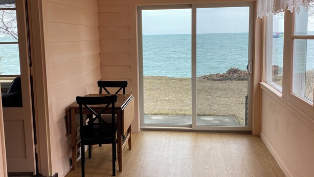 Ein Zimmer mit Holzboden, einem Tisch mit Stühlen und einer großen Schiebeglastür mit Blick auf einen Strand.