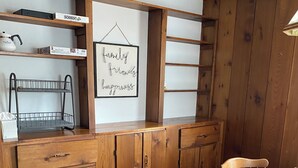 Ein Essbereich mit Holzboden, einem runden Tisch, vier Stühlen, einem Metallregal und einem gerahmten Schild an der Wand.