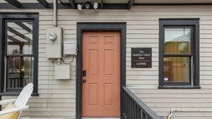 A house with a brown door, a sign reading "The Maida Vale Flats Lover," and a white rocking chair on the porch. - Spacious main level 2 bdrm off Missoula Hip Strip, across river from downtown (Missoula)