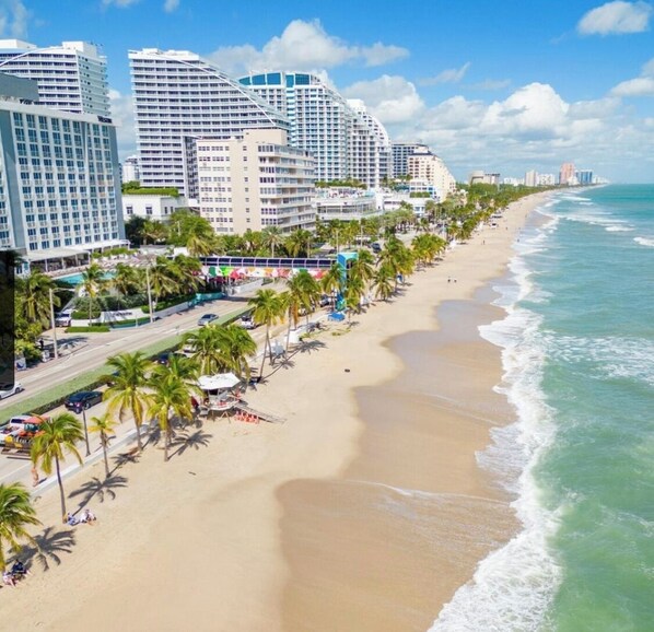 A beachfront hotel with multiple high-rise buildings, a sandy beach, and palm trees.