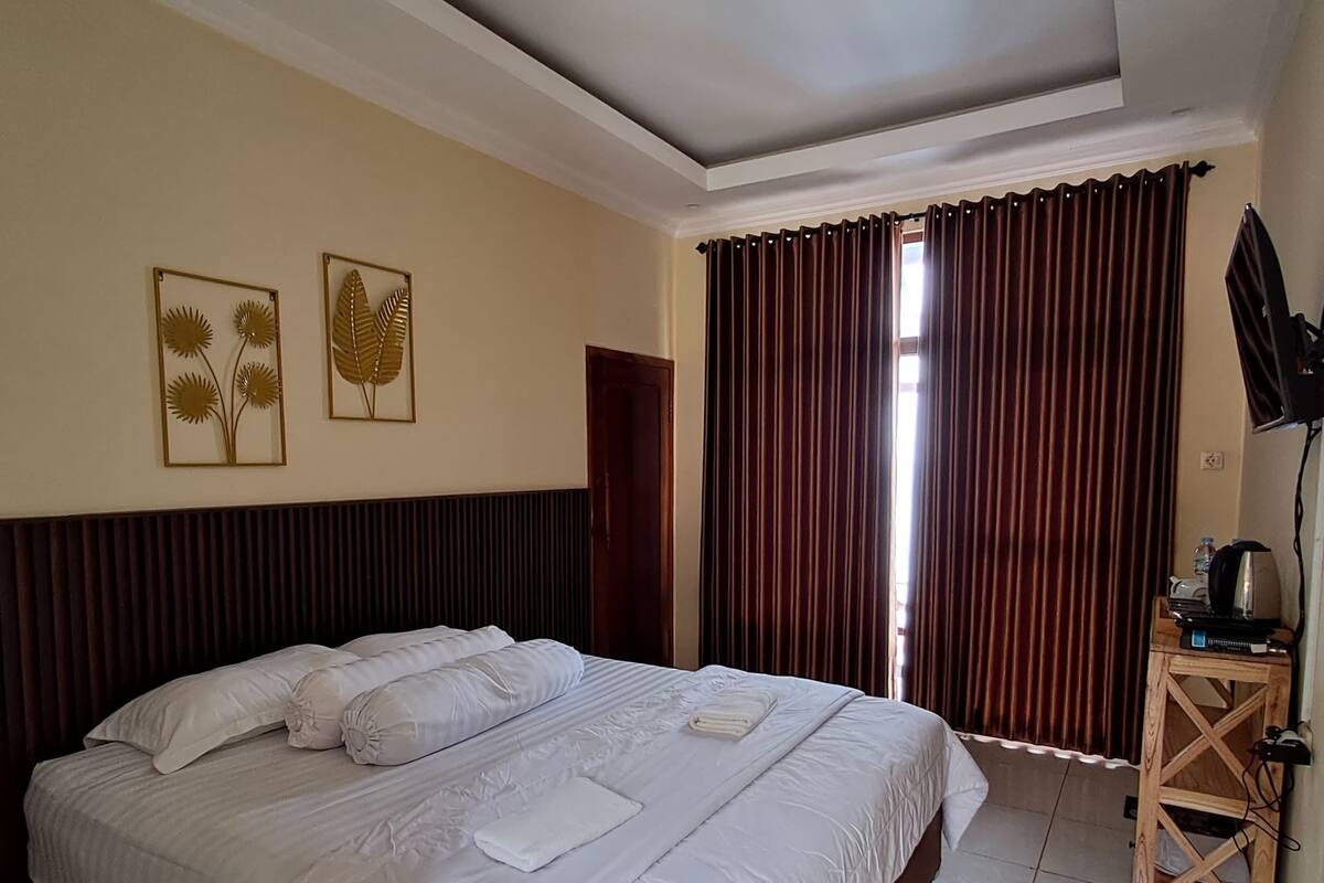 A hotel room with a large bed, a desk with a computer, and a window with curtains.