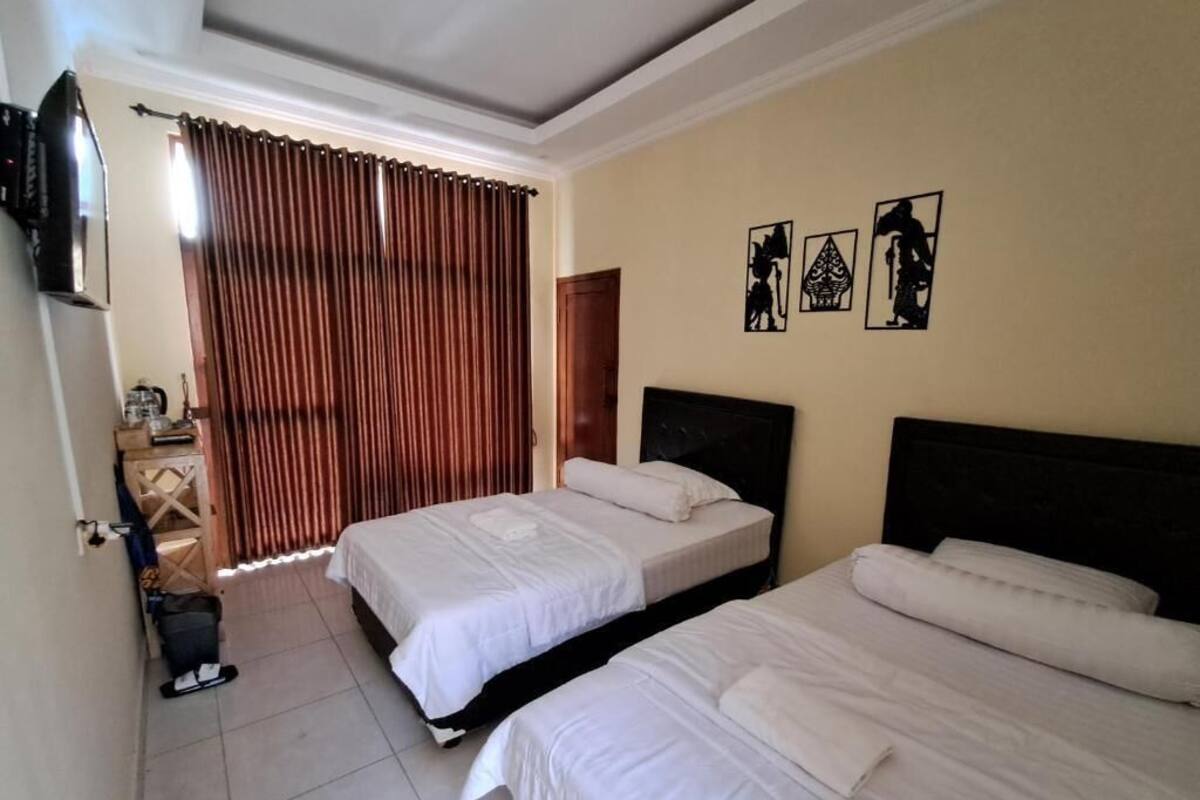 A hotel room with two beds, a television, a window with curtains, and artwork on the wall.