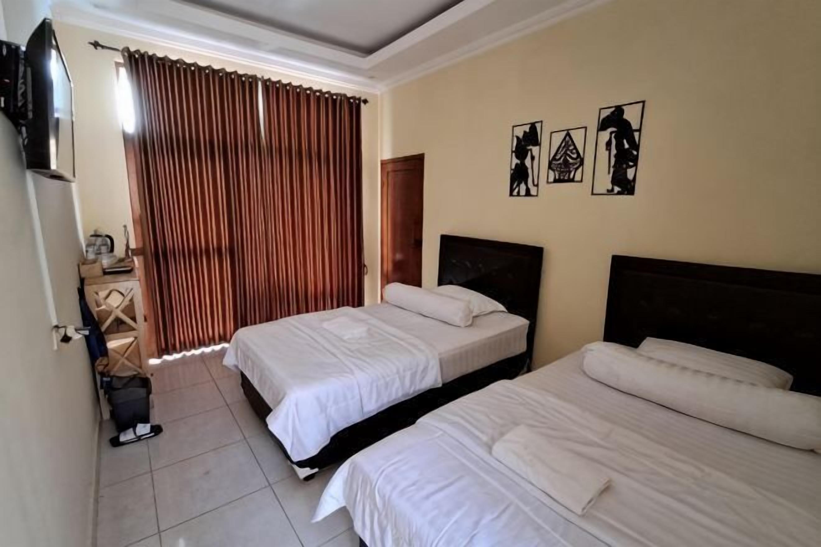 A hotel room with two beds, a desk, a chair, a TV, and a window with curtains.