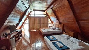 A room with a sloped ceiling, wooden walls, a bed with pillows, a TV, and a small table with a kettle. - Teras Kaca (Panggang)