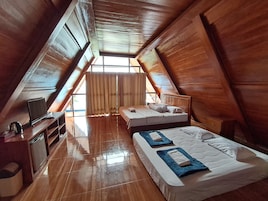 Quarto com teto inclinado, paredes de madeira, cama com almofadas, televisão e uma pequena mesa com chaleira.