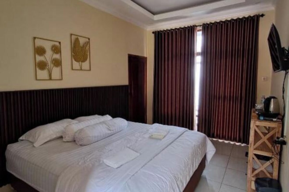 Una habitación de hotel con una cama grande, dos obras de arte en la pared, una ventana con cortinas y una pequeña mesa de madera con un televisor.