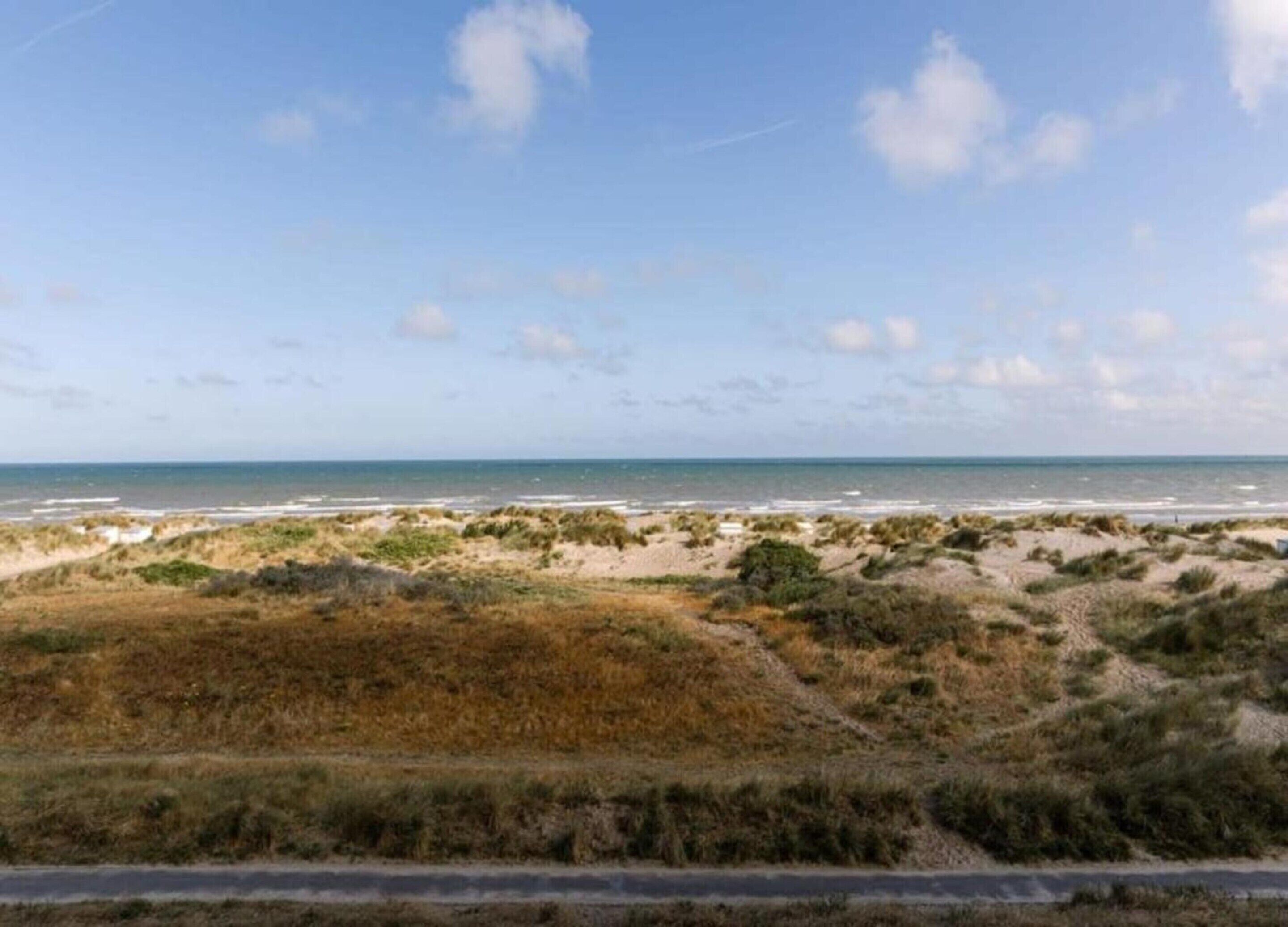 A coastal landscape with dunes, beach, and a clear sky.