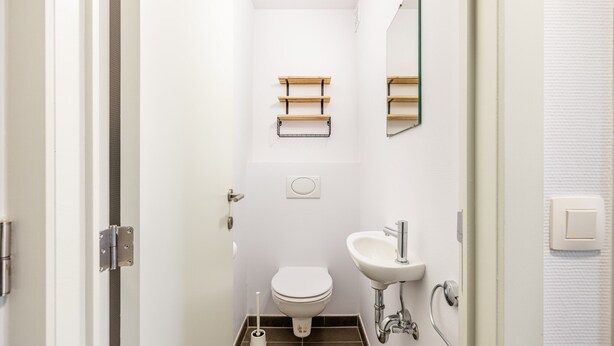 A narrow bathroom with a toilet, sink, and towel racks. - Apartment in Koksijde Near the Beach (Koksijde)
