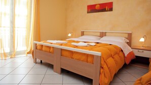 A neatly made bed with an orange blanket and white pillows, a wooden headboard, and a nightstand with a lamp. - B&B Casa Mauro (Linguaglossa)