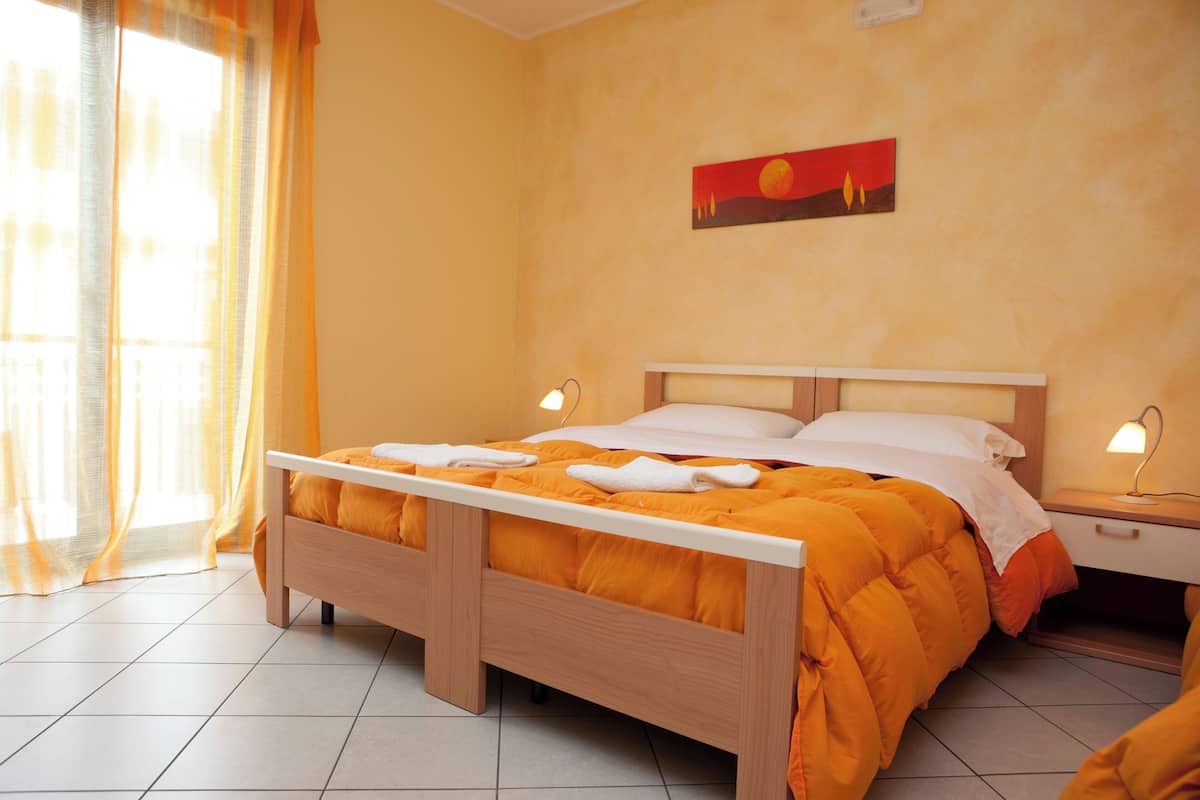 A neatly made bed with an orange blanket and white pillows, a wooden headboard, and a nightstand with a lamp.