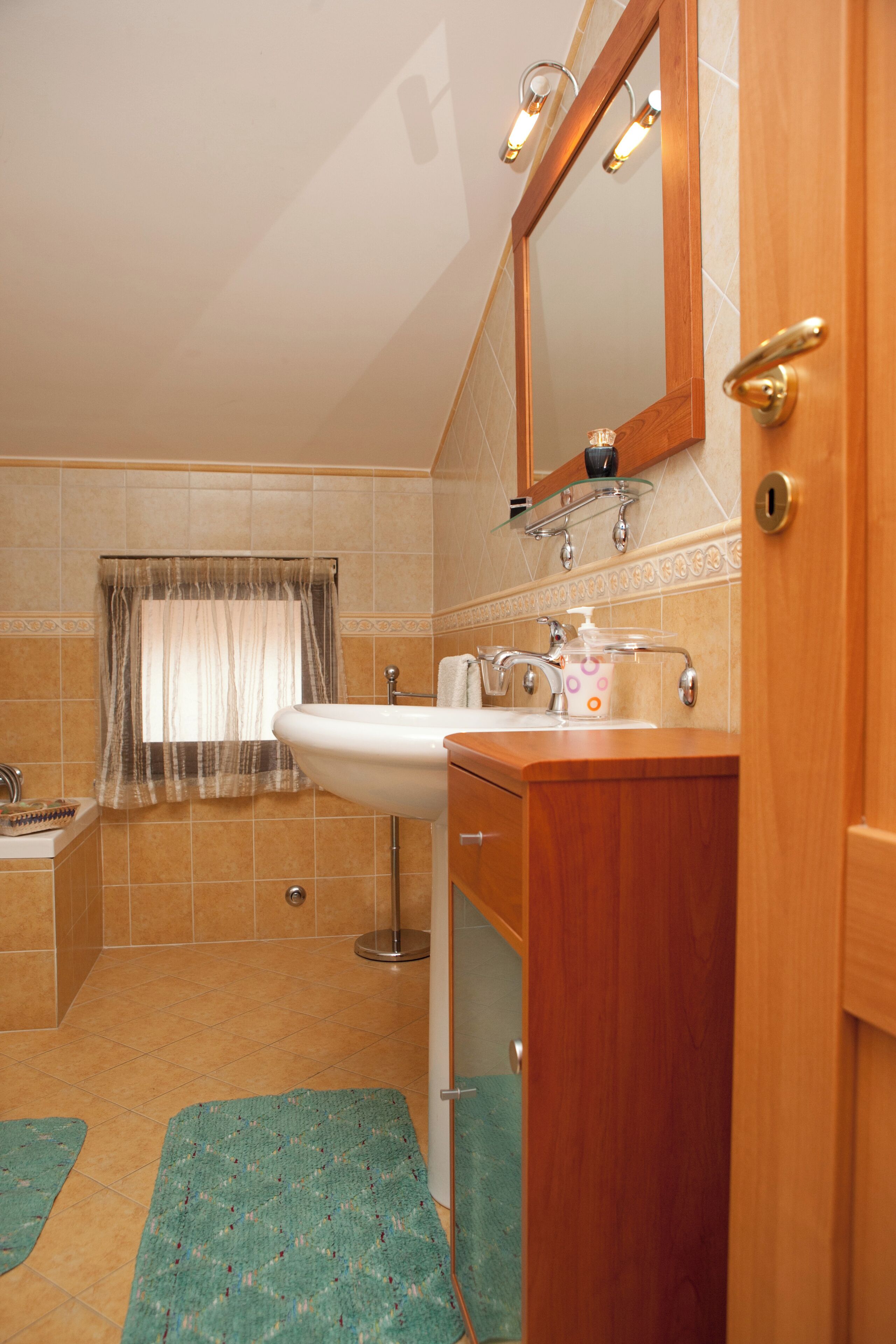 A bathroom with a wooden vanity, a sink, a mirror, and a window with a curtain.