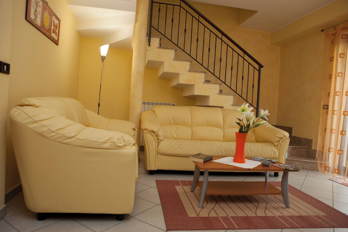 A living room with two yellow sofas, a coffee table, and a staircase.