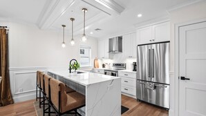 Una cocina moderna con armarios blancos, un refrigerador de acero inoxidable grande y una isla de mármol.