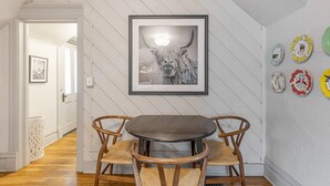 A dining area with a round table and two chairs, a framed picture on the wall, and decorative plates.