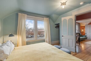 Un dormitorio con cama, ventana con cortinas, lámpara y vistas al exterior.