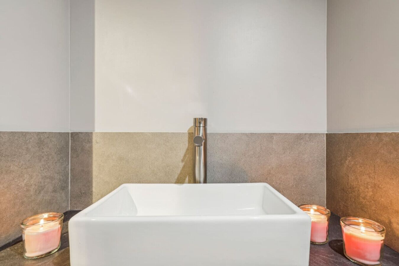 A modern bathroom with a white sink, a chrome faucet, and two lit candles on the counter.