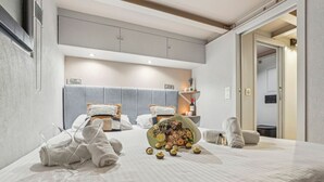 A hotel room with a large bed, two bedside tables, a grey headboard, and a small bathroom visible through an open door.