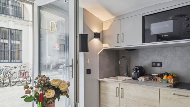 A modern kitchen with a Bosch microwave, a sink, and a coffee machine. There is a vase with flowers on the windowsill.