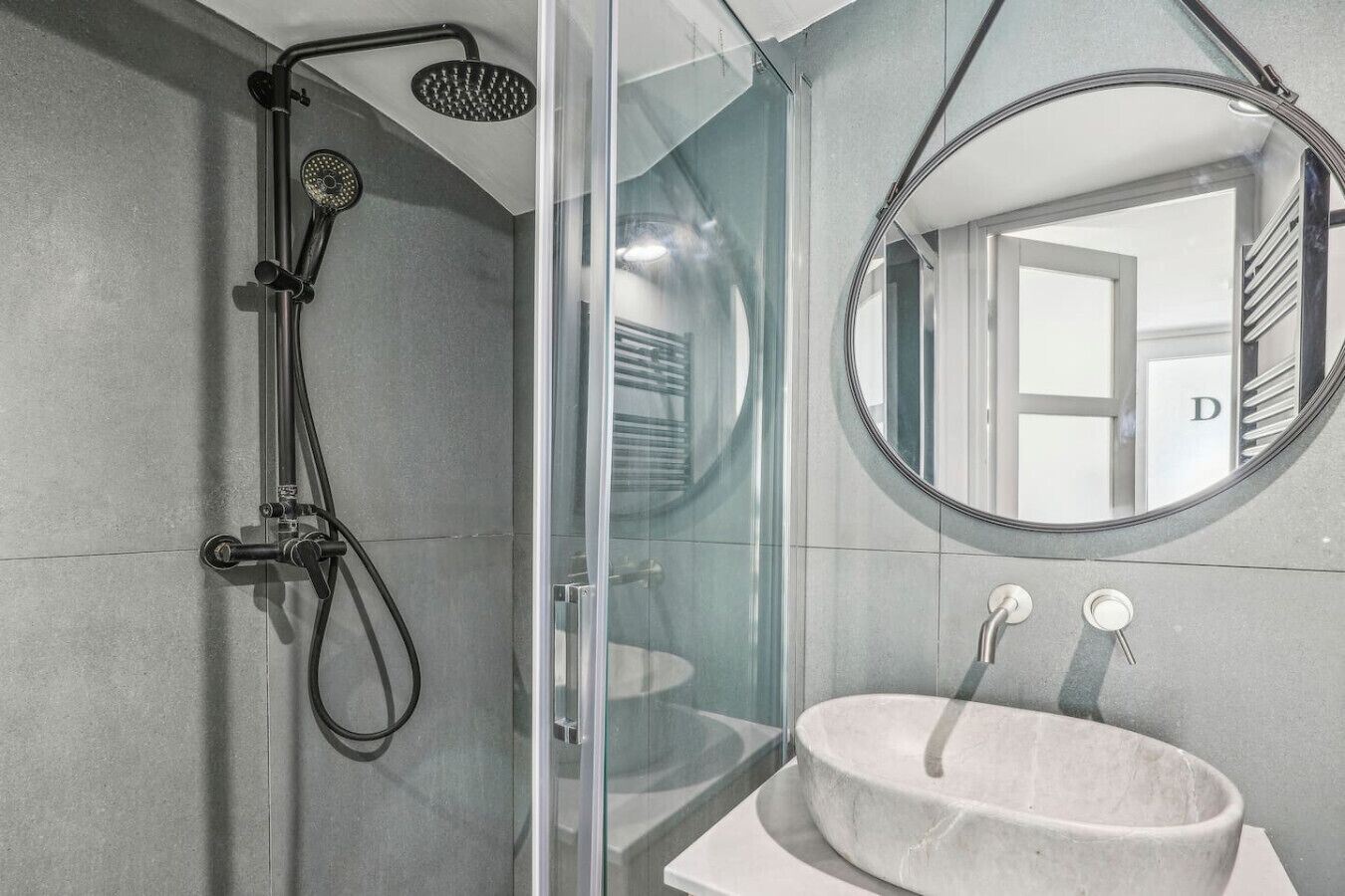 Une salle de bain moderne avec une douche à parois de verre, un miroir rond et un lavabo sur colonne.