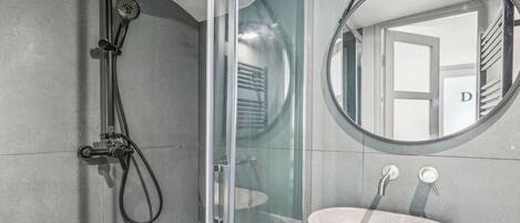 Une salle de bain moderne avec une douche à parois de verre, un miroir rond et un lavabo sur colonne.