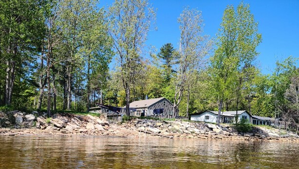 A lakeside cabin with a dock extending into the water, surrounded by trees and a rocky shoreline.