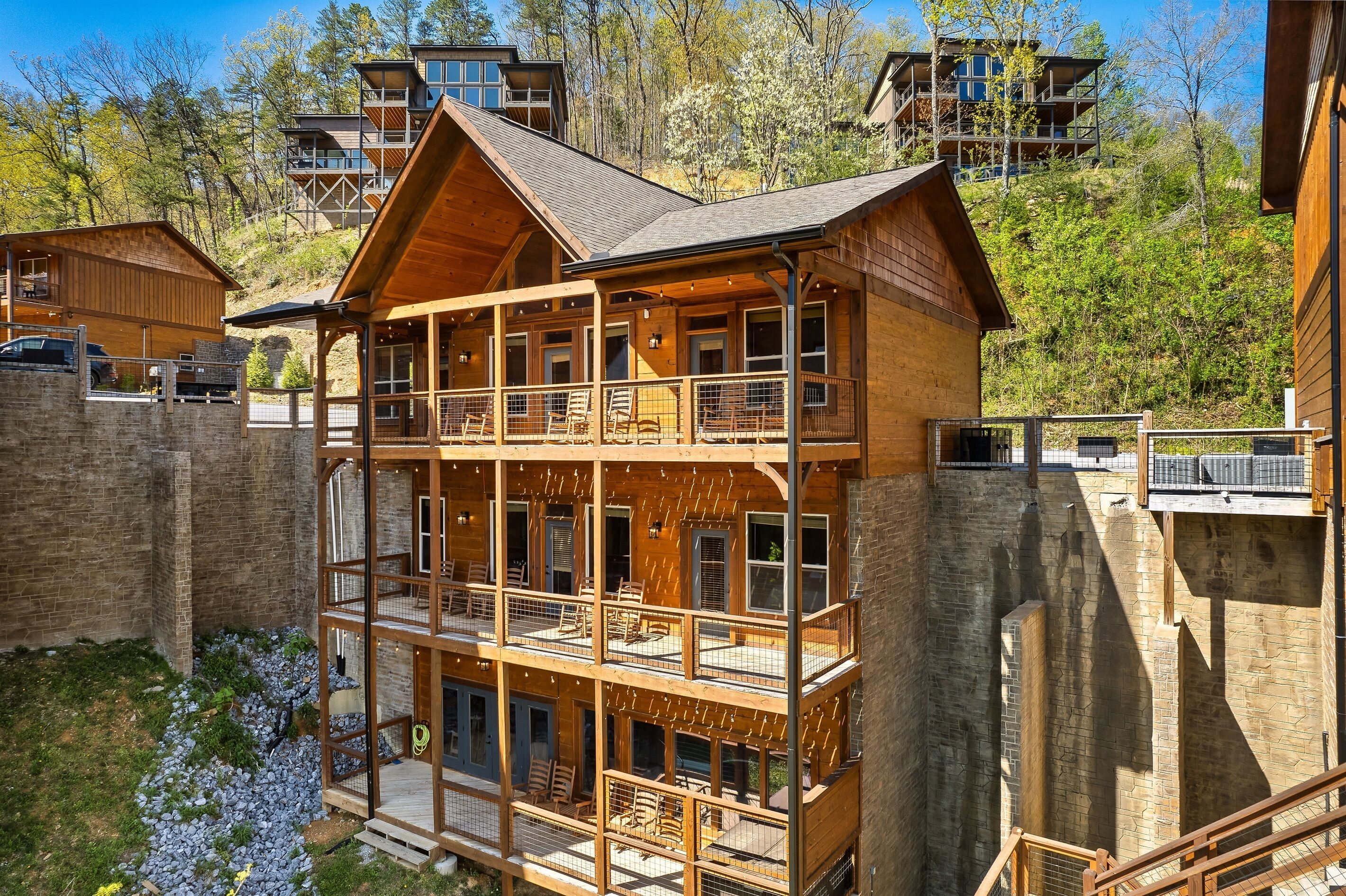 A multi-story wooden cabin with balconies, surrounded by a stone wall and set in a wooded area.
