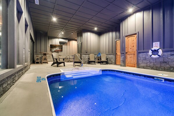 An indoor swimming pool with a clear blue water surface, surrounded by a stone wall and wooden doors. - FreeDollywood Tix,HeatedPool,HotTub,Gameroom,Views (Sevierville)