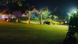 A nighttime outdoor area with a lawn, a motorcycle, and illuminated decorations. - ARAVALI HILLS RESORT  (Sohna)
