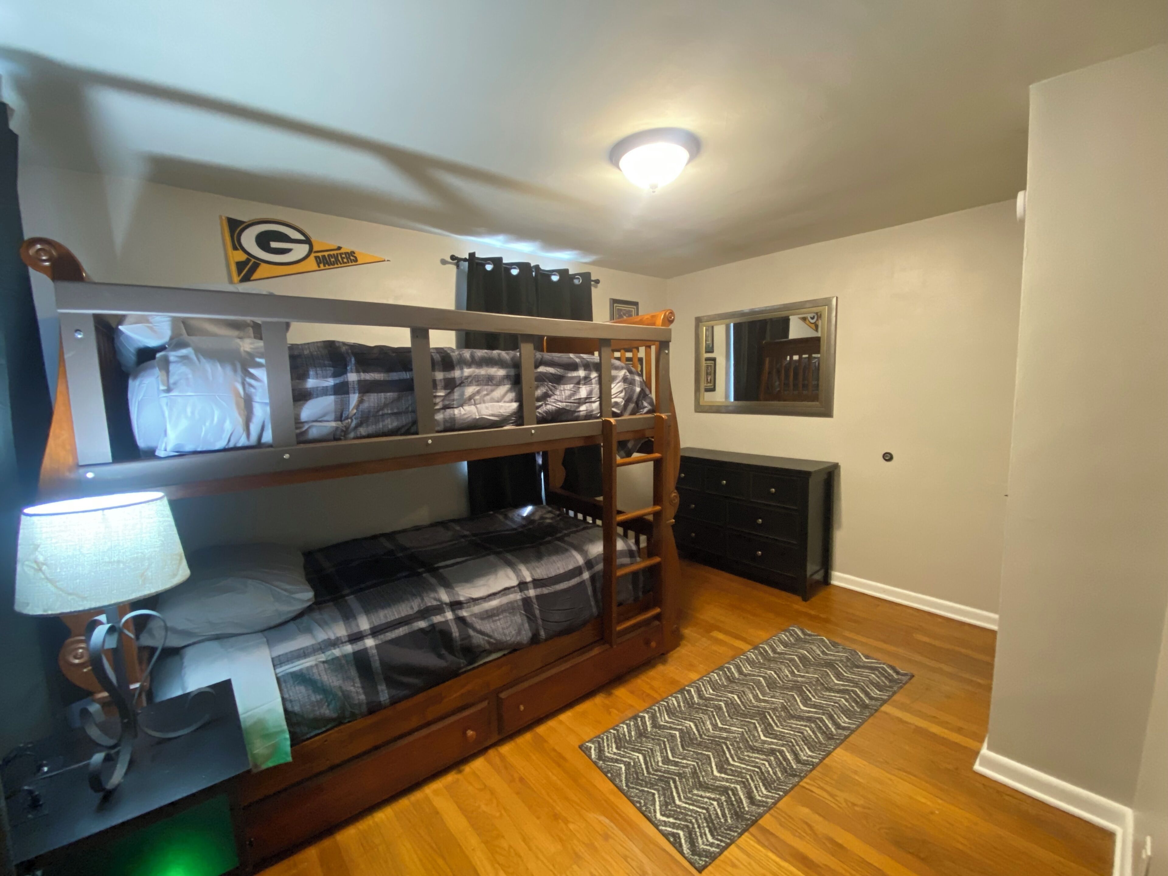 A bunk bed room with a lamp, a dresser, a mirror, and a ceiling light.