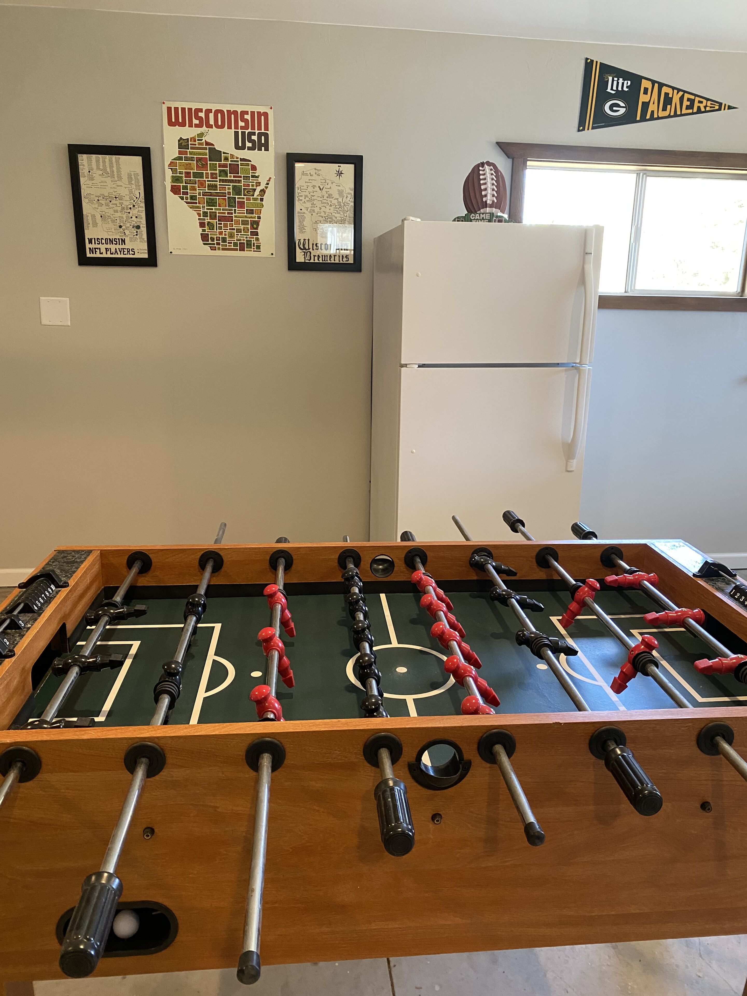A foosball table in a room with a refrigerator and framed posters on the wall.