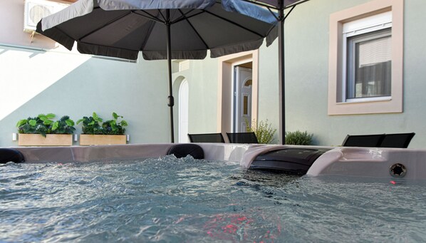 A hot tub with a view of a building, outdoor seating, and potted plants.