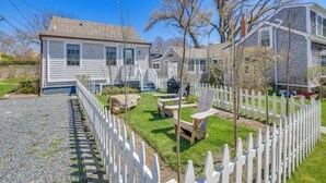 Una propiedad residencial con entrada de grava, cerca blanca enrejada y césped con mobiliario exterior.