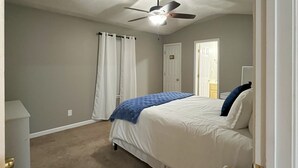 Een slaapkamer met een bed, een plafondventilator, een deur en een nachtkastje.